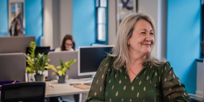 A smiling woman in a green blouse sits at a laptop