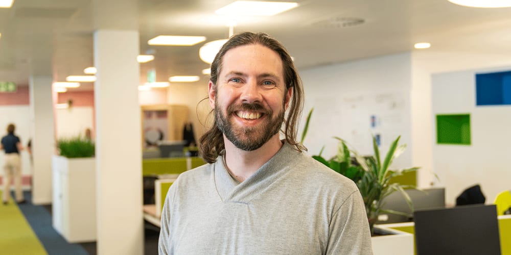 A photo of Alex smiling with the FreeAgent office in the background.